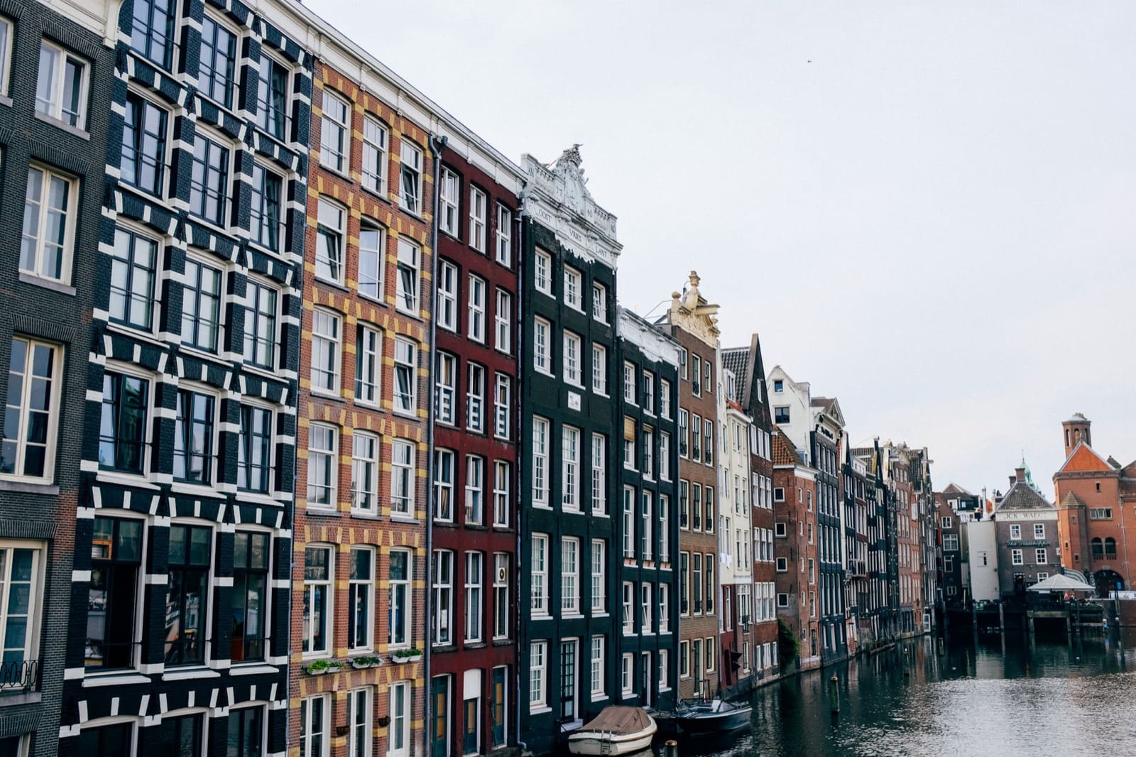Exterior of narrow multicolored apartment houses without balconies overseeing canal with modern boats moored near entrances