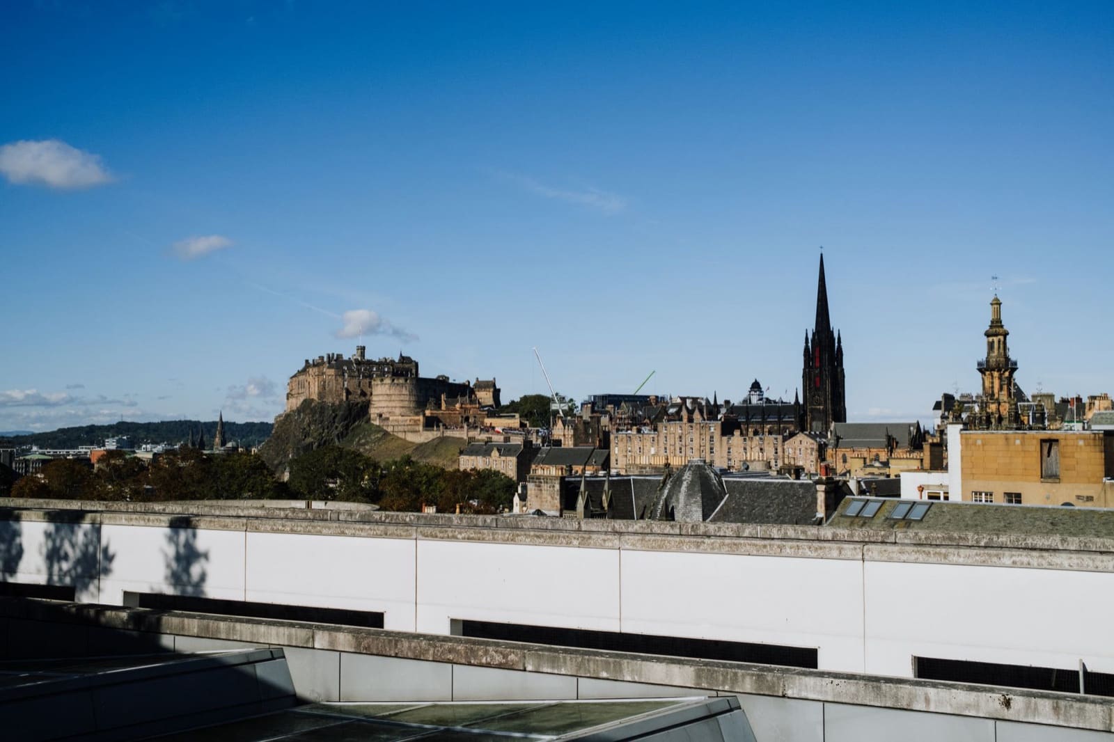 A scenic daytime view of Edinburgh Castle and skyline, under a clear blue sky.