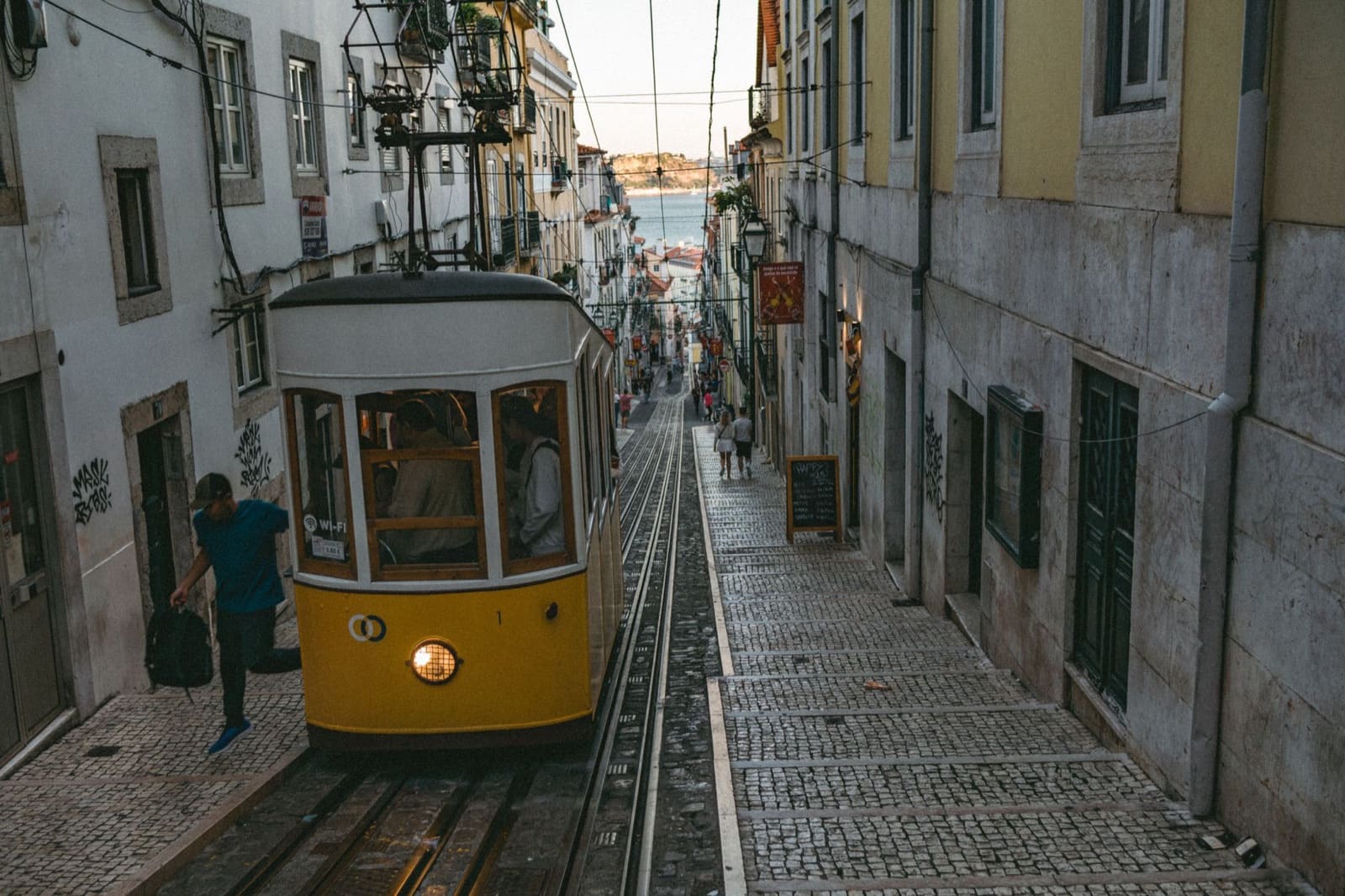 Vintage tram navigates a quaint cobblestone street in Lisbon, Portugal, capturing urban charm.